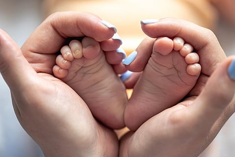 Mom holds the legs of a newborn baby in her hands
