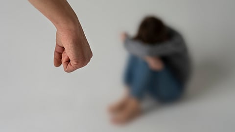 A blurred image of a girl child sitting in a corner and a forearm of a man indicating abuse against the child.
