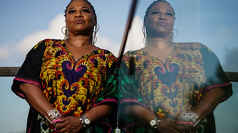 Image of a woman standing by a window wearing a printed kaftan, with her shadow visible on the glass.