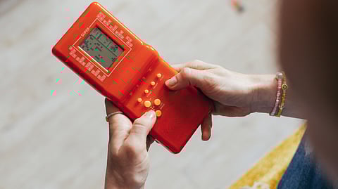 Image of a person playing Tetris in an orange colored device.
