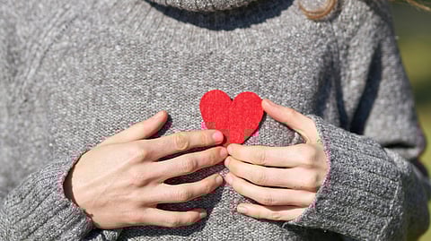 Image of a woman wearing a grey sweater and holding a paper heart in her hands.