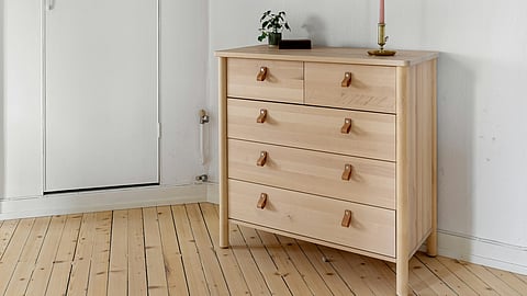 A wooden chest of drawers stands in a room, showcasing its natural finish and classic design.