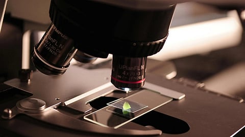 Image of a microscope focusing on a slide.