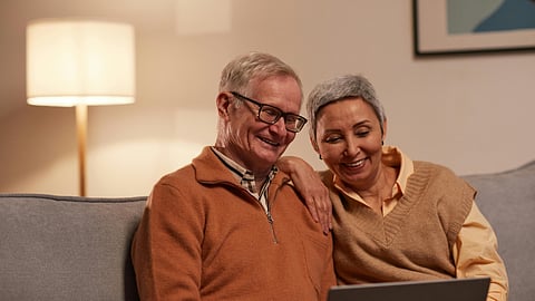 An older couple sits together on a couch, using a laptop and sharing a moment of connection and engagement.