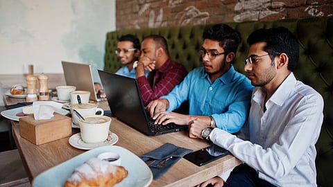 A group of young Indians working in laptops with coffee and croissants on the table.