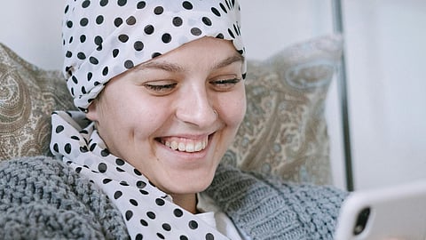 A smiling woman wearing a head scarf is engaged with a tablet, showcasing her enjoyment of technology.