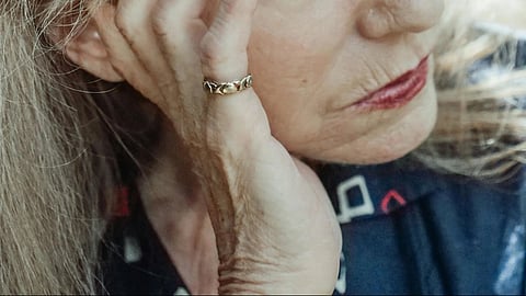 Image of a woman's hand over her face wearing a dark brown lipstick.