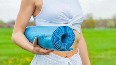Image of a woman wearing white sports set and holding a blue yoga mat.