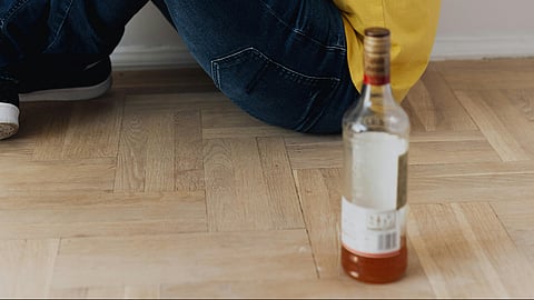 A man on the floor with his hands raised, possibly in a gesture of  surrender with alcoholism as alcoholic beverage bottle is near. him.

