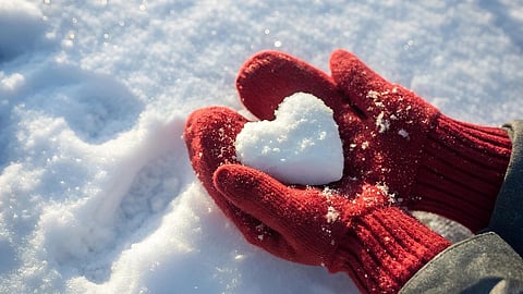 Two hands in red gloves create a heart shape in fresh white snow