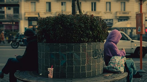 Image of 2 people sitting at the opposite side of a seating space at the side of the road.