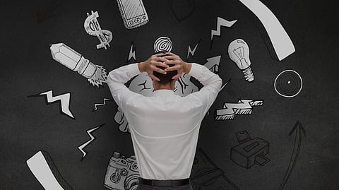 A man holding his head facing a black wall with few diagrams of bulb, rocket, money etc.
