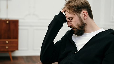Image of a man wearing a black jacket sitting in a room in disheartened expressions.