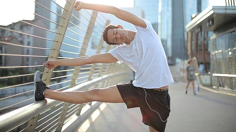 Image of a man wearing white t-shirt and black shorts doing yoga on the side of a bridge.