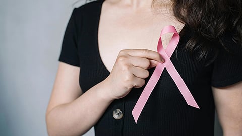  A woman holds a pink ribbon in her hand, symbolizing support for breast cancer awareness.