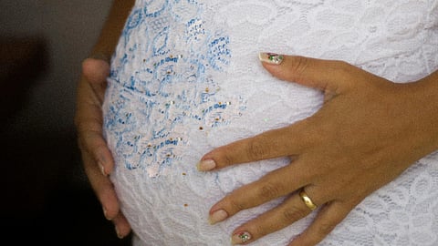 Image of a pregnant woman wearing a white dress having her hands over her belly.