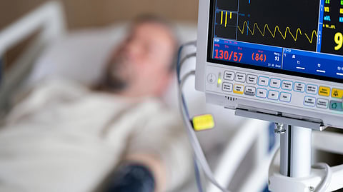 A man lying in a hospital bed, monitored by an ECG machine displaying his heart activity.