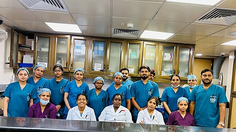 A group of nurses in blue scrubs is posing for a photo.   Some of them are standing and some are sitting.