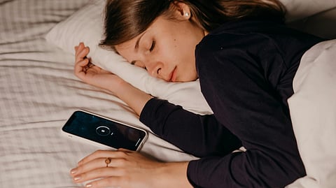 A woman asleep in bed, her phone placed on the nightstand next to her.