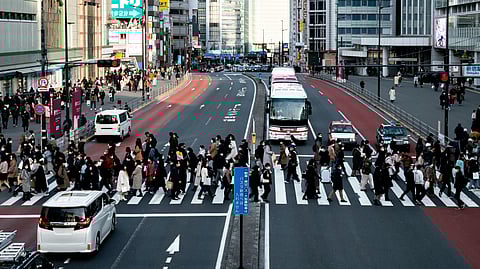 A large group of people is crossing the zebra crossing in a huge intersection. 