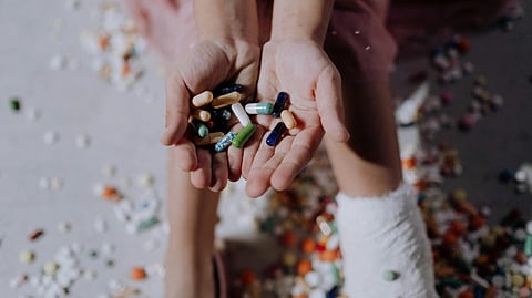 Image of two people with one placing their hand over the other, holding antibiotics, with more pills scattered in the background.
