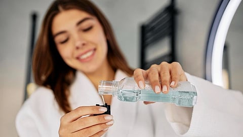 A woman in a white bath robe is pouring a mouthwash into its cap before using it.