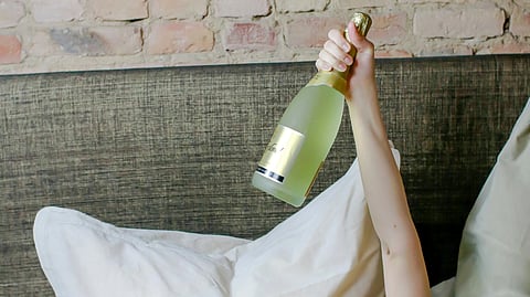 A woman relaxing in bed with a bottle of champagne beside her, creating a cozy and celebratory atmosphere.