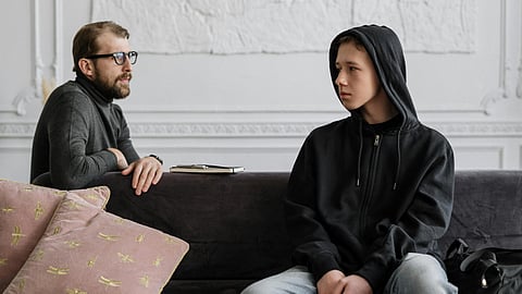 Two men sitting on a couch, relaxed, with a decorative pillow between them.