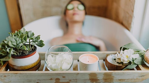 A woman relaxes in a bathtub surrounded by candles and lush green plants, creating a serene and tranquil atmosphere.