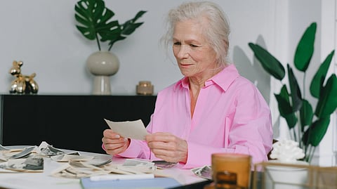 Image of an old woman wearing a pink top seeing photographs.