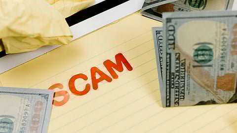 An image of SCAM written on a paper with currency notes around.