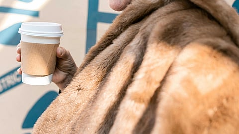 Image of a woman wearing a scarf and holding a cup of coffee.
