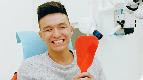 An image of a patient checking his teeth in mirror at dental office.