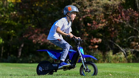 A boy rides a blue dirt bike across a grassy field, showcasing his skills and enjoying the outdoor adventure.