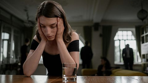 An image of a girl sitting at a table looking distressed with her face in her hands.