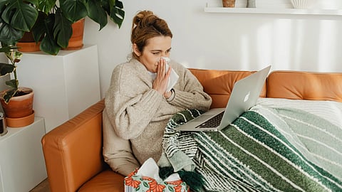 An image of a woman sitting on couch with tissues suffering from flu.