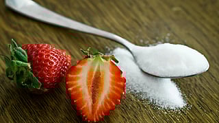 Image of a spoon having sugar along with strawberries.
