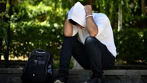Image of a guy sitting sadly wearing a white hoodie in a park.