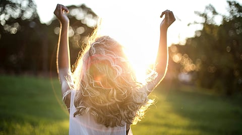 Image of a woman with blonde curly hair, facing the sunlight in the early morning.