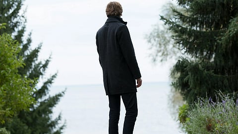 A man in a suit walks confidently down a tree-lined path, surrounded by greenery.