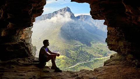 Image of a man sitting on a large rock, surrounded by natural scenery.