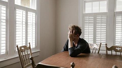 An image of a man looking out of the window in very depress mood.