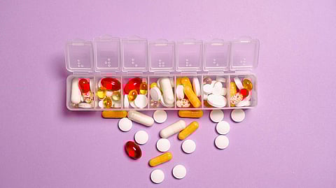 Image of different types of tablets and capsules in a box in front of a purple background.