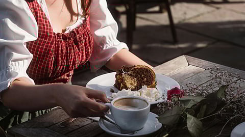 Image of a woman sitting at a table, enjoying a slice of cake and a cup of coffee.