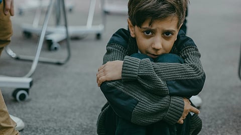 A young boy sitting on the library floor, surrounded by books, focused on reading a storybook.