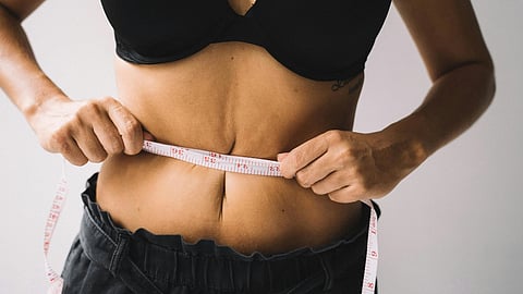 A woman in a black bra top measuring her waist with a tape measure, focused on her fitness routine.