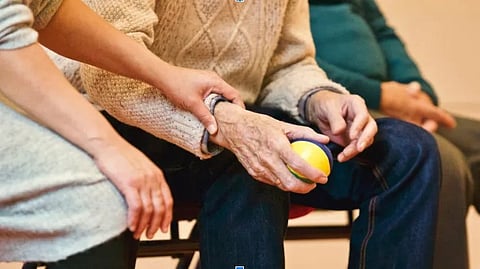A person holds a ball in front of an elderly individual, engaging in a playful interaction.