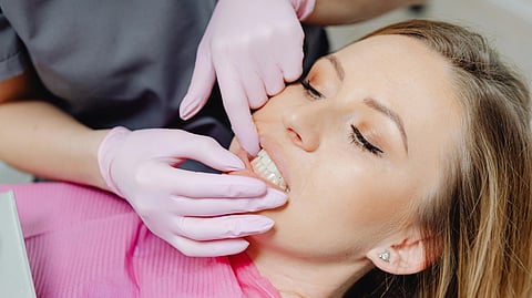 A woman sits in a dental chair while a dentist cleans her teeth with dental tools.