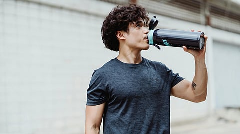 A man takes a sip from a black sports bottle while outdoors.