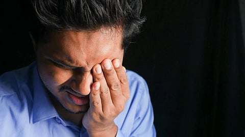 Image of a person wearing a blue shirt suffering from eye irritation.
